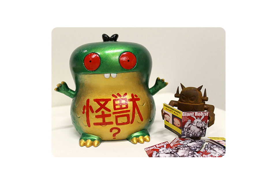Larger green frog-like figure and smaller robot-like figure reading a magazine/comic book